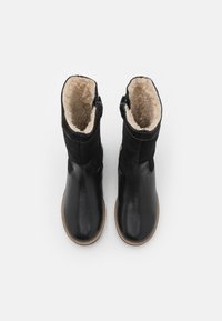 Botas de invierno de cuero negro con costuras marrones y forro de vellón beige, vistas desde arriba sobre un fondo blanco.