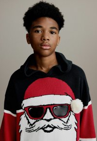 Rode en zwarte gebreide trui met een ontwerp van een Santa-gezicht, dat een zonnebril en een witte pompon op de borst heeft. Geribbelde kraagdetails.