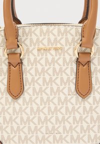 Sac fourre-tout beige avec un motif intégral affichant les initiales "MK". Il est orné d'accents en cuir marron et de ferrures dorées.