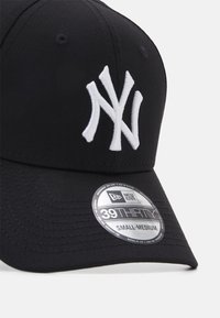 Juodas kepurė su struktūrizuotu dizainu, ant kurios yra iškeltas baltas siuvinėtas "NY" logotipas. Pridedama sidabrinė "New Era" etiketė su užrašu "39THIRTY SMALL-MEDIUM."