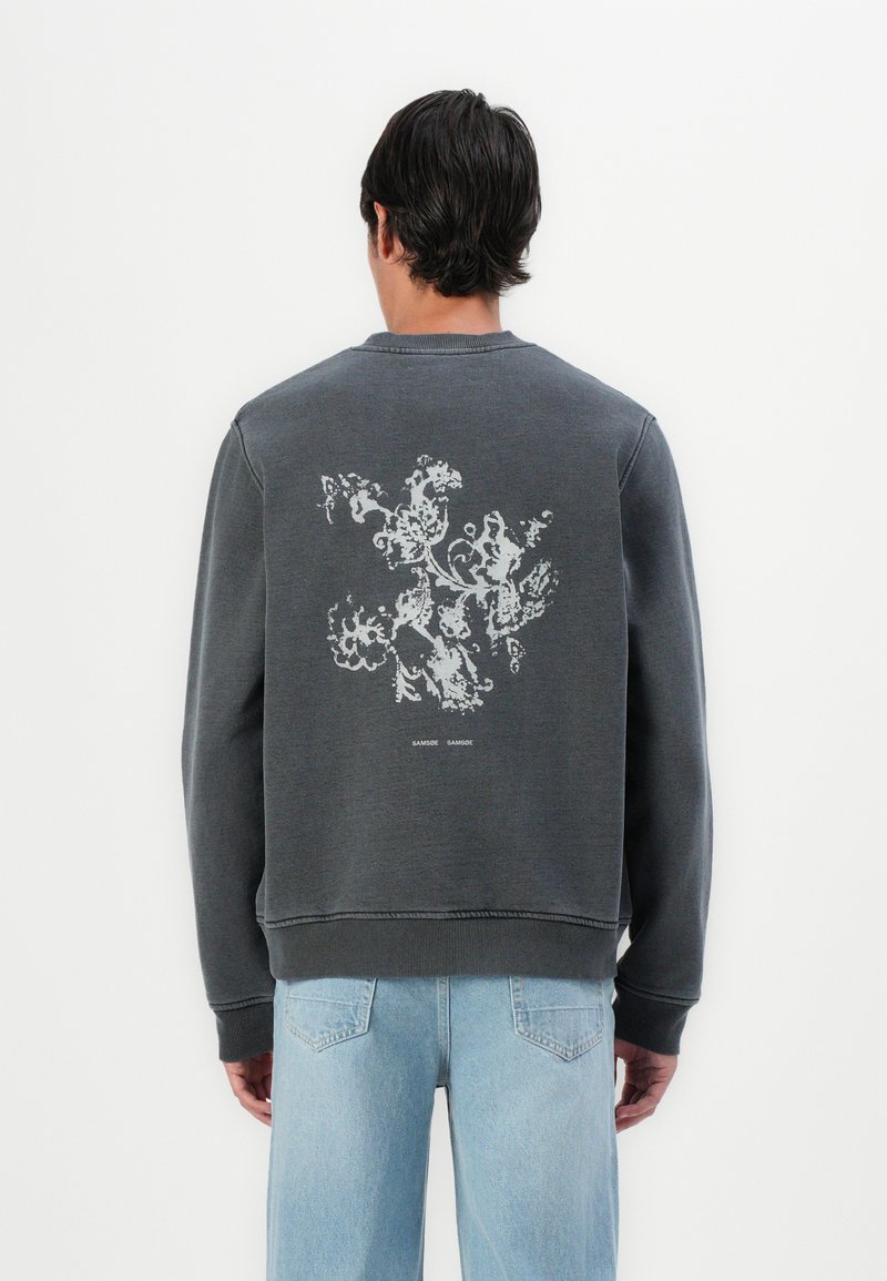 Tricou gri cu guler rotund, care prezintă un print floral alb texturat pe spate. Manșete și tiv cu nervuri, croială lejeră și material moale.