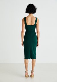 Grön figursydd klänning med breda axelband, medellång, slät textur, har en dragkedja bak, matchad med sandaler med strappy högklack.