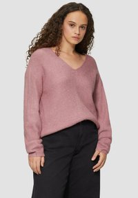 Lichtroze gebreide trui met een V-hals, lange mouwen en een ontspannen pasvorm, gecombineerd met zwarte wijduitlopende broek. Getextureerde stof, minimale details.
