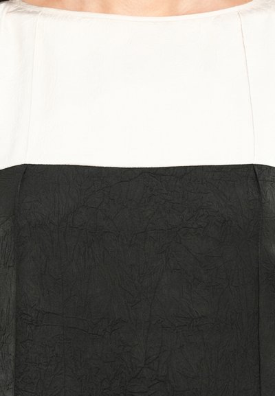 Mustvalge kleit, millel on must, tekstuuriga alakülg ja sile valge üleosa, millel on lai kaelus ja kortsus kangadetail.