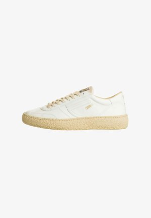 Sneaker bianca low-top con suola beige testurizzata, lacci beige e marchio dorato discreto su lato e linguetta.