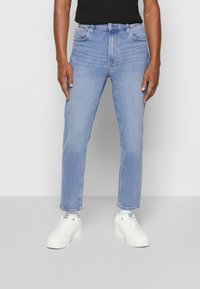 Ljust blå denimjeans med rak passform, femficksdesign och subtil blekning, tillsammans med vita sneakers.