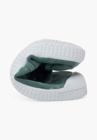 Zapatilla de tela verde con suela de goma blanca y un patrón de agarre texturizado, doblada para mostrar los detalles del interior y las costuras.