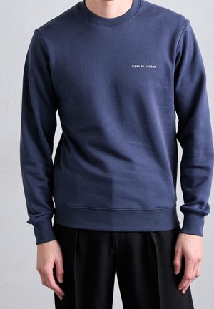 Donkerblauwe sweatshirt van zacht materiaal, met een ronde hals en ribgebreide manchetten. Het logo "Tiger of Sweden" in het wit op de borst.