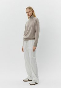 Pulover bej cu guler înalt dintr-un material moale, asortat cu pantaloni albi cu dungi. Pantofii sunt de culoare deschisă și au un design simplu.