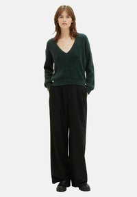 Groene, gestructureerde V-hals trui gecombineerd met losse zwarte broeken en zwarte schoenen. De outfit heeft lange mouwen en een ontspannen pasvorm.