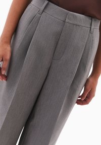 Szare dopasowane spodnie z teksturowanej tkaniny, z plisami z przodu, bocznymi kieszeniami i czystym krojem.