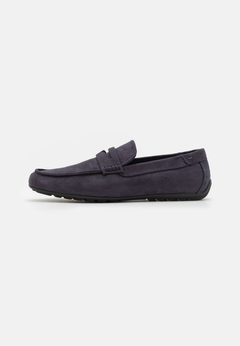 Mocassins en daim bleu marine, avec un design de style mocassin, présentant un accent cousu et une semelle en caoutchouc flexible pour plus de confort.
