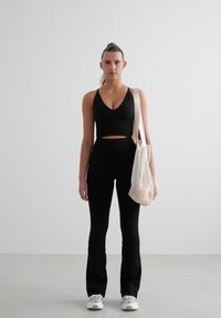 Musta lyhyt toppi ja korkeavyötäröiset mustat leveälahkeiset housut, joilla on sileä pinta. Vaaleanbeige olkalaukku yksinkertaisella designilla. Harmaat lenkkarit korostuksilla.