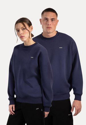 Felpe blu navy con collo a giro, polsini a coste e un piccolo logo ricamato sul petto. Esibite su un modello maschile e un modello femminile.