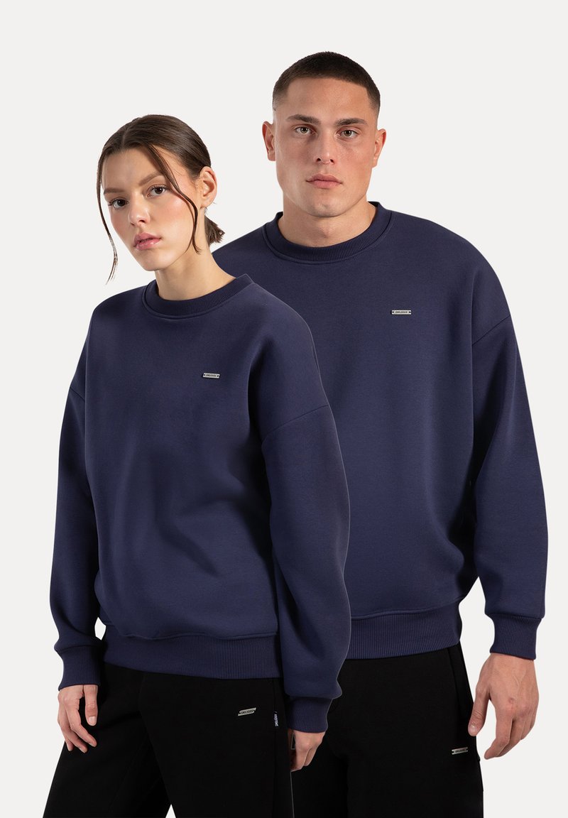 Felpe blu navy con collo a giro, polsini a coste e un piccolo logo ricamato sul petto. Esibite su un modello maschile e un modello femminile.