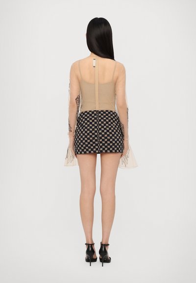 Top a maniche lunghe in rete trasparente con dettagli ricamati, abbinato a una mini gonna a scacchi bianca e nera. Modella indossa tacchi neri.