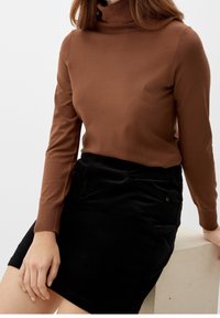 Brauner, enganliegender Rollkragenpullover mit langen Ärmeln, kombiniert mit einem schwarzen Cordrock. Glatte Textur mit subtilen Stickdetails.