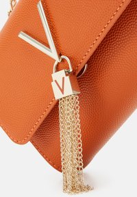 Orange texturerad handväska med detaljer i guldkedja. Har en metallisk V-formad accent och ett guld-lås med V-logotyp. Kompakt design.