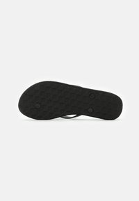 Semelle de sandal noire avec un motif texturé. Comprend deux impressions circulaires et un bord lisse. Fabriquée en matériau durable, au design plat.