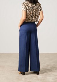 Breda marint tygbyxor med blå ränder, tillverkade av ett strukturerat material. Har hög midja och fickor, tillsammans med en mönstrad topp.