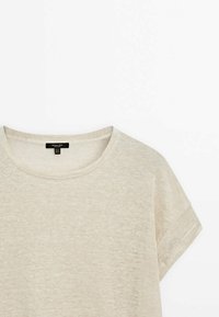 T-shirt beige a maniche corte realizzato in un tessuto leggero; presenta un colletto rotondo e maniche arrotolate; leggera trama visibile.