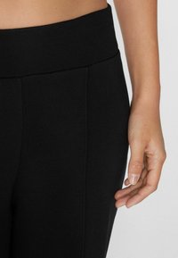 Schwarze Leggings mit einem dicken, elastischen Bund. Glatte Textur mit vertikalen Nähdetails an den Seiten. Keine sichtbaren Muster oder Beschläge.