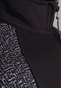 Chaqueta atlética negra con un alto cuello, tejido texturizado en un lado y material suave en el otro para contraste.