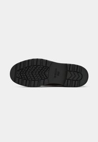 Black rubber shoe sole with a textured tread pattern, featuring zigzag and circular grip designs. Includes embossed brand name detail.