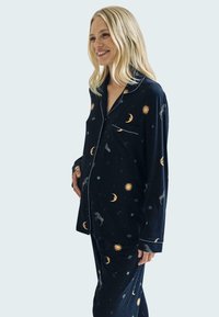 Conjunto de pijama navy en tejido suave que presenta patrones celestiales, incluyendo lunas y soles. El diseño incluye una parte superior con botones y pantalones a juego.