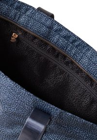 Blau gemusterte Handtasche mit einer Reißverschluss-Innentasche; das Innere besteht aus einem strukturierten schwarzen Material und einem goldenen Reißverschluss.