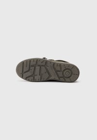 Suola della scarpa, materiale in gomma, con texture e modelli di grip, prevalentemente grigia con accenti di verde; dettaglio del logo circolare vicino al tallone.