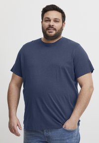 Tamsiai mėlyna trumpa rankovė marškinėliai su apvalia iškirpte, pagaminti iš minkštos medžiagos, derinami su šviesiai mėlynomis džinsomis. Paprastas, nepuošnus dizainas.