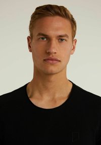 Černé tričko s kulatým výstřihem vyrobené z hladké látky, s malým, decentním logem na levé straně hrudi.
