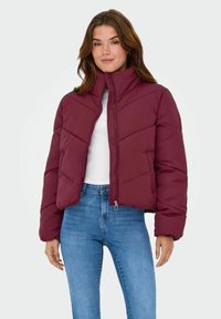 Bordo puf jakna s visokim ovratnikom, s prešanim uzorkom i zatvaranjem na zip, uparena s svijetloplavim uskim trapericama.