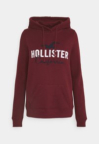 Felpa con cappuccio bordeaux con coulisse, tasca anteriore e scritta ricamata "HOLLISTER California" in bianco e blu. Tessuto morbido in misto cotone.