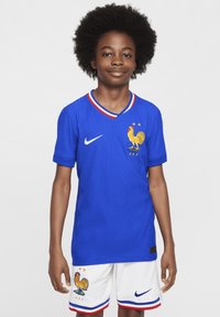 Camiseta de fútbol Nike azul con textura acanalada, con un emblema de gallo y tres estrellas. Pantalones cortos blancos con acentos similares.