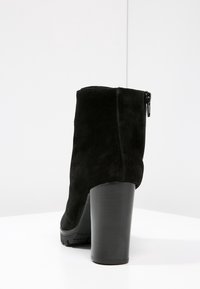 Bottine en suède noir avec un talon épais et une fermeture éclair sur le côté, dotée d'une finition texturée et d'un talon lisse pour la stabilité et l'adhérence.