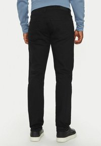 Pantaloni in denim neri con vestibilità slim, caratterizzati da una vita a media altezza, design a cinque tasche e una texture liscia. Abbinati a sneaker nere.