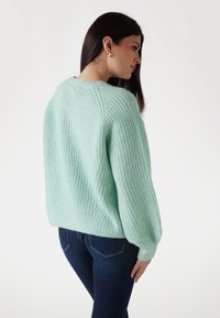 Minzgrüner, gestrickter Pullover mit langen, gepufften Ärmeln und einem gerippten Muster. Verfügt über einen runden Halsausschnitt und ein kleines Detail auf der Rückseite.