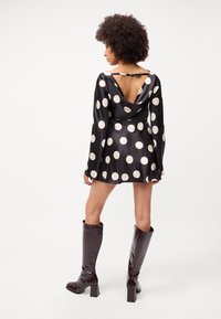 Rochie din satin negru cu buline albe, mâneci lungi, decolteu adânc la spate și fustă evazată. Asortată cu cizme lucioase de burgund înalte.