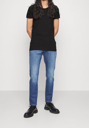 Černé tričko s krátkým rukávem, světle modré džínové kalhoty a černé šněrovací boty s robustní podrážkou. Jednoduchý design bez viditelných vzorů nebo ozdob.