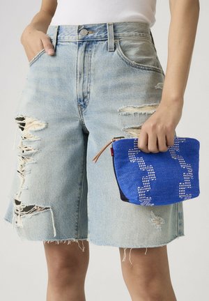 Person wearing light blue ripped denim shorts and holding a small blue patterned fabric pouch with a brown zipper pull.