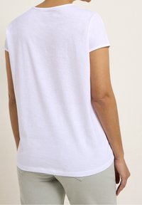 T-shirt bianco a maniche corte con scollatura rotonda e vestibilità rilassata. Il tessuto appare morbido e leggero, con una texture liscia.