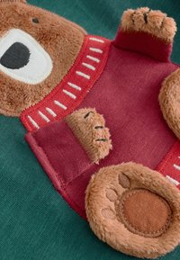 Motivo di orso bruno in tessuto morbido con texture marroni e rosse, caratterizzato da dettagli ricamati e uno sfondo verde.