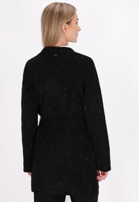 Zwarte cardigan met een ontspannen pasvorm, gemaakt van textuurstof met witte spikkels, om de taille gestrikt, met lange mouwen en zijsplitten.