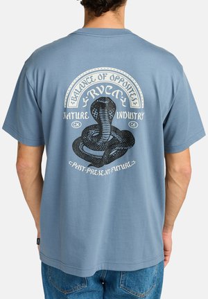 Camiseta de algodón azul con mangas cortas, que presenta un gráfico de una serpiente y texto en la parte posterior. Corte relajado y dobladillo sencillo.