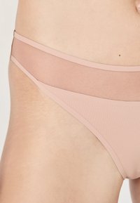 Bikini bottom nudo con una texture liscia, caratterizzato da una vita in rete trasparente a contrasto e un design minimalista.