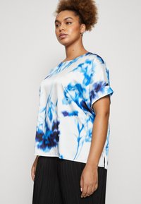Satin t-skjorte med korte ermer i hvit med blå og mørkeblå tie-dye mønstre, rund hals og sideslisser.