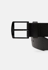 Ceinture en cuir noir avec une finition texturée, une boucle rectangulaire en métal argenté avec un logo, et une boucle pour l'ajustement.
