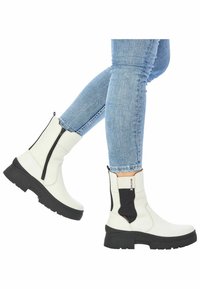 White ankle boots with a side zipper, rubber sole, and black stretch panel. Smooth texture, rounded toe, and chunky heel design.
